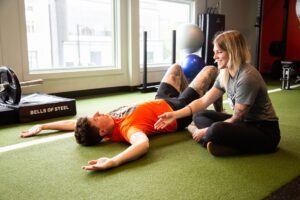 man laying on the ground next to a MYo Lab therapist receiving physical therapy in MYo Lab Health & Wellness center