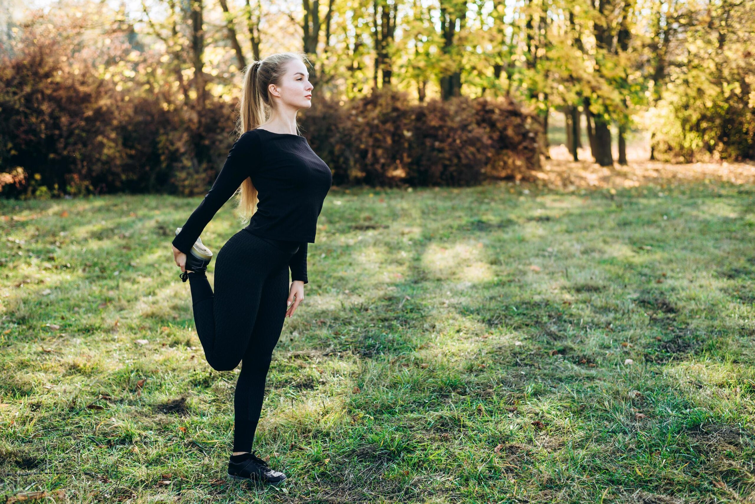 woman dressed in black training clothes stretching in a field