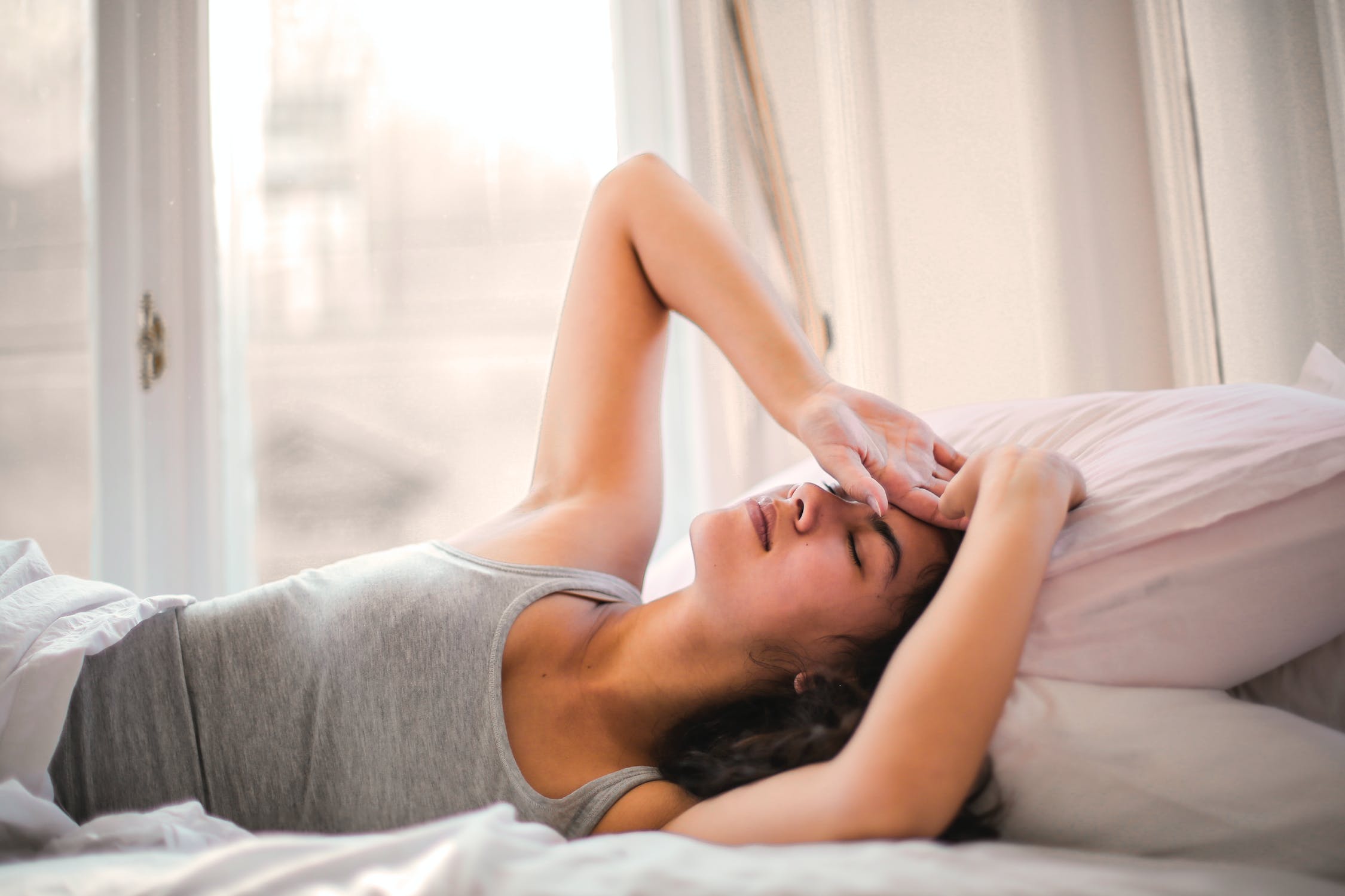Woman lying down waking up with a headache. Why do I wake up with a headache?