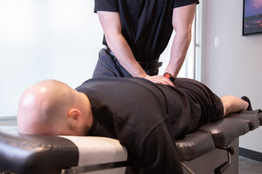 Chiropractor providing hands-on lower back treatment to a patient lying face down on a treatment table.