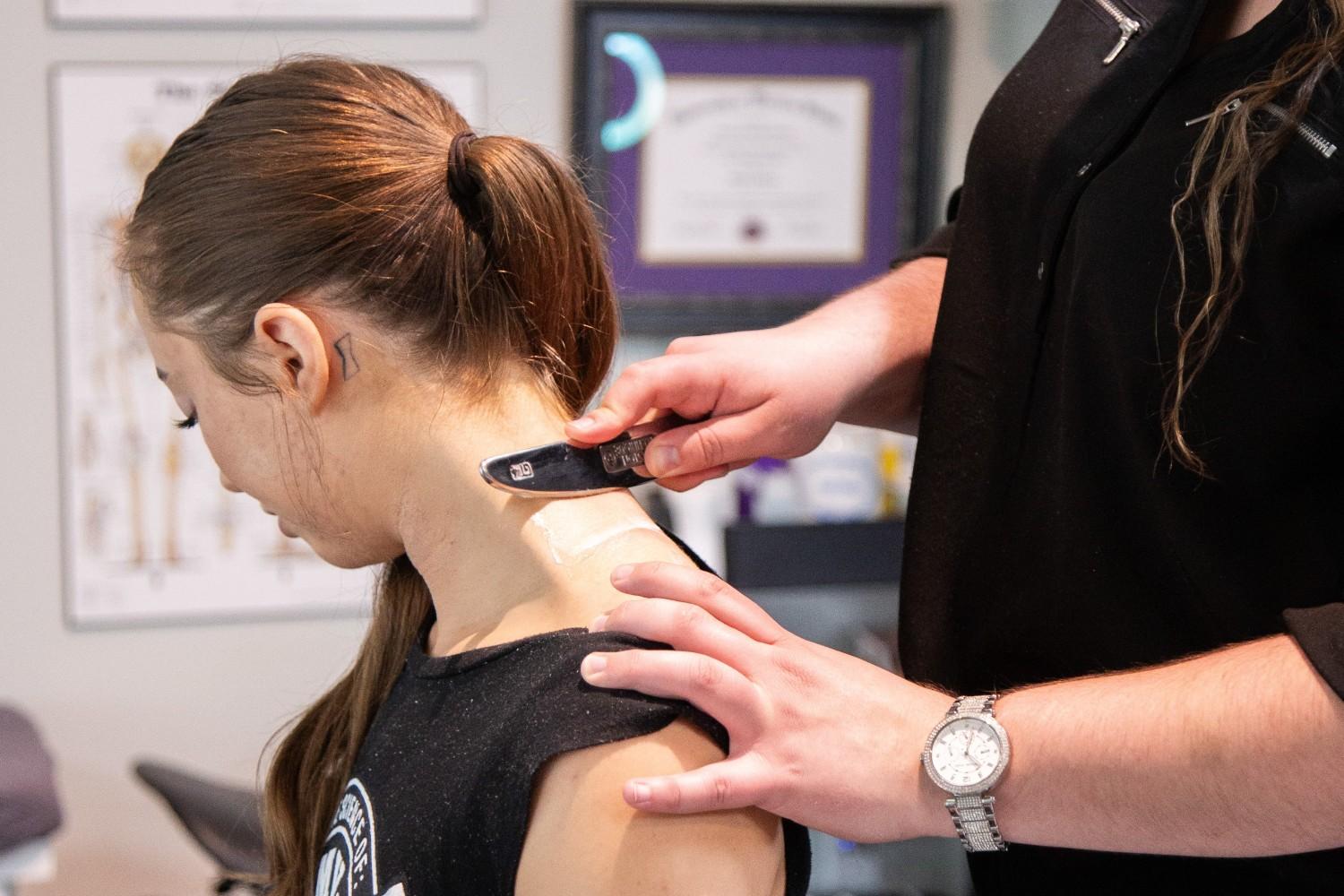 A therapist at MYo Lab Health & Wellness using the Graston Technique to treat neck muscles with a specialized instrument.