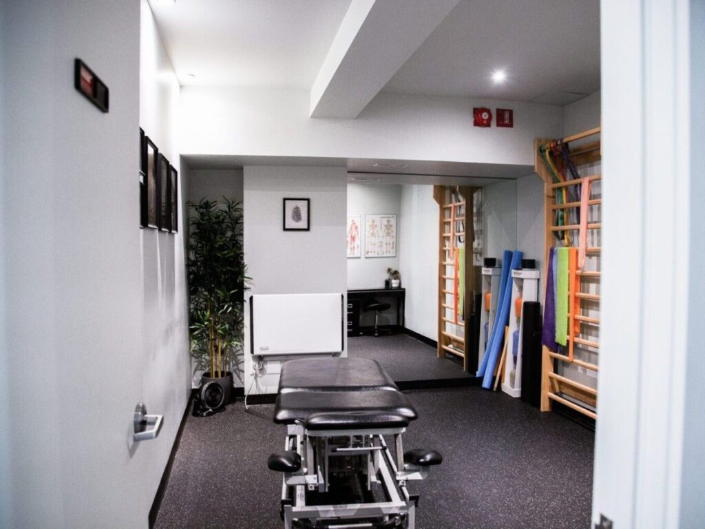 A clean, modern schroth therapy room featuring a treatment table, wall bars, exercise equipment, and plants, inviting a therapeutic atmosphere.