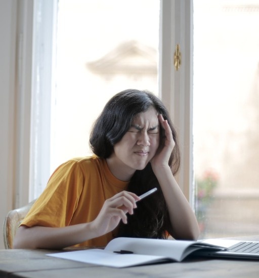 Woman experiencing headache and head tension while working at a desk, commonly linked to stress, posture, or neck strain.