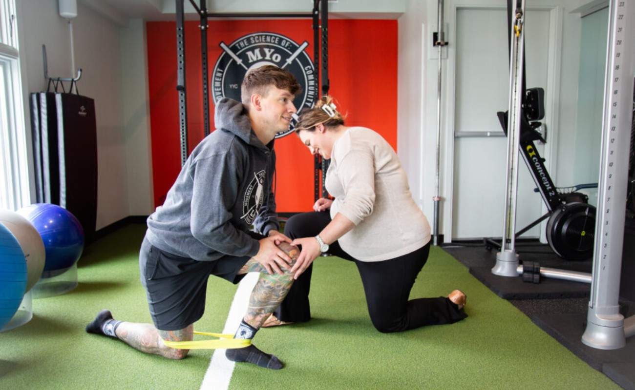 Coach guides knee rehab assessment with resistance band at MYo Lab in Calgary.